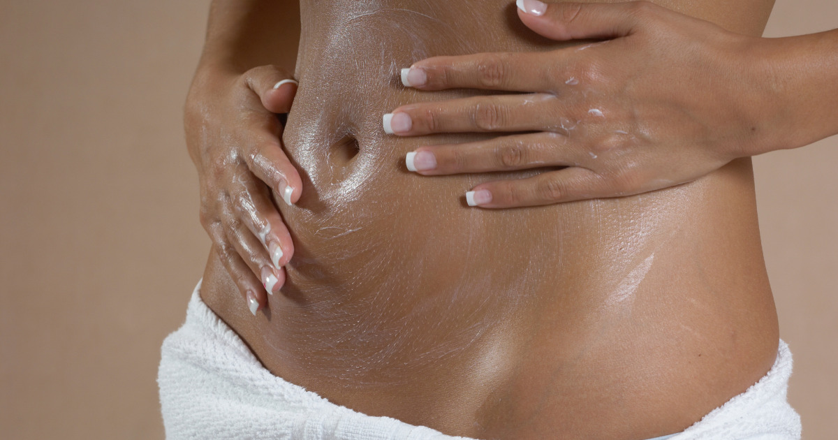 woman rubbing lotion on their stomach